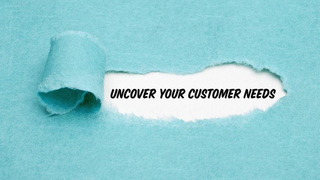 Image of piece of blue paper with a piece peeled back to reveal "Uncover Your Customer Needs." This illustrates customer interviewing tecniques that can help founders uncover meaningful data